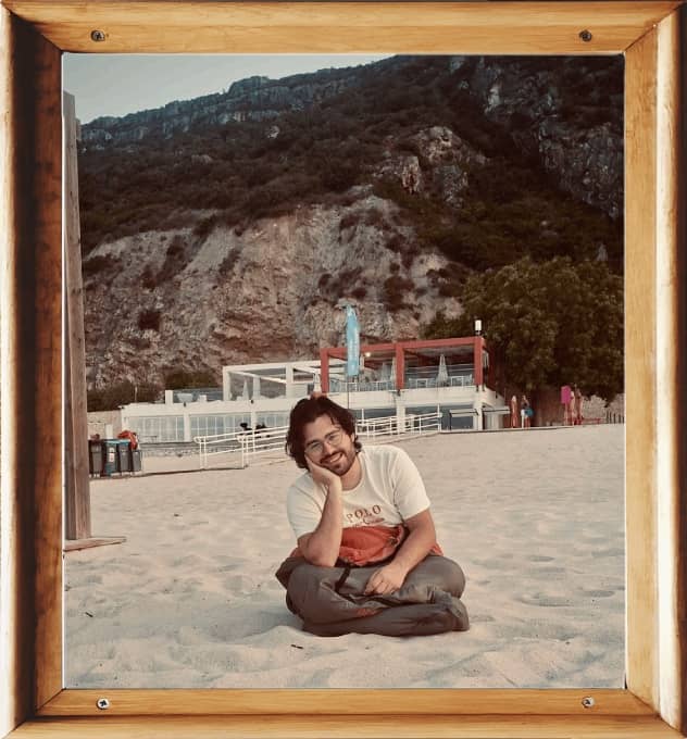 Gabe Fernando smiling inside a sleeping bag while sat on a beach